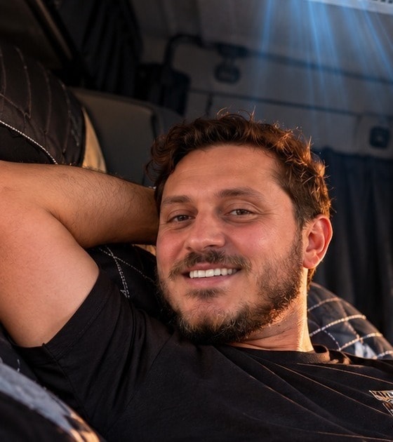 Sampaio sorrindo, deitado e relaxado na cabine-leito do caminhão, com a mão atrás da cabeça